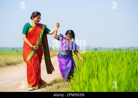 Tracking shot, ragazza bambino giocare toccando raccolto tenendo la mano madre a terra agricola - concetto di cura dei genitori. Foto Stock