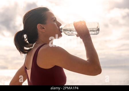 Donna sportiva che prende una bevanda d'acqua da una bottiglia dopo aver raggiunto o eseguito fuori. Foto Stock