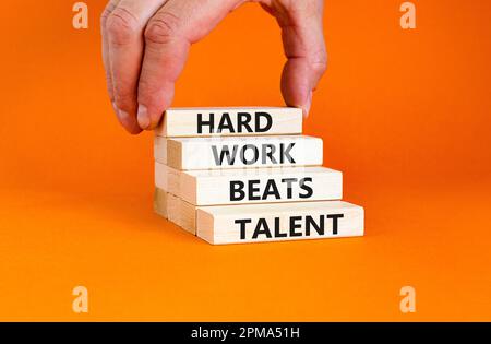 Il duro lavoro batte il simbolo del talento. Concetto parole duro lavoro batte talento su blocco di legno. Bella tavola arancione sfondo arancione. Business motivazionale h Foto Stock