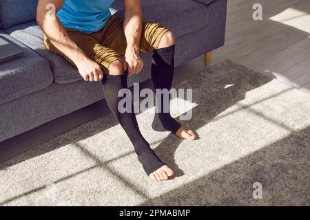 Giovane uomo con trombosi o varicose mette su calze di compressione medica allungabile Foto Stock