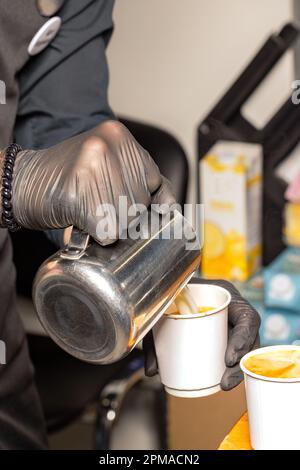 Un barista professionista versa il latte in una tazza di carta da caffè mentre prepara un cappuccino. Primo piano, immago verticale. Foto Stock