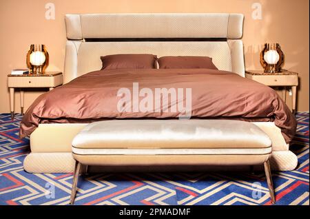 Un letto matrimoniale con testiera in morbido velluto, comodini dorati con splendide lampade e soffice piumone marrone. Foto Stock