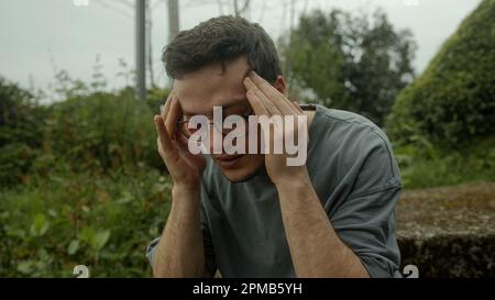Giovane uomo con gli occhiali che torce nel dolore, combattendo un improvviso insorgere di problemi di salute Foto Stock