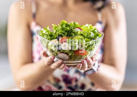 Una giovane donna tiene una sana insalata di primavera in una ciotola di vetro. Foto Stock