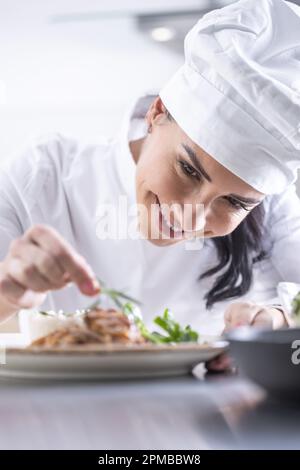 Una giovane cuoca femminile finisce il pasto con erbe nella cucina del ristorante - primo piano. Foto Stock