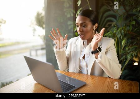 Felice scioccato la donna d'affari afroamericana millenaria in vestito bianco ha videochiamata sul laptop in caffè Foto Stock