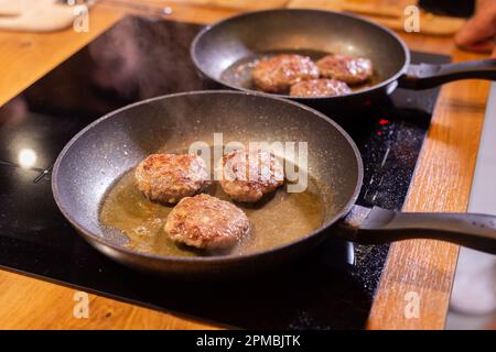 Hamburger di carne o tortino a forma di cotoletta che vengono fritti poco a poco in olio su una padella Foto Stock