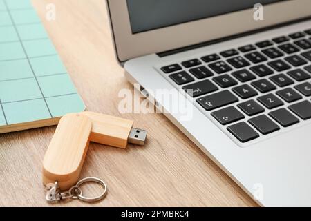 Moderno computer portatile con unità flash USB su sfondo in legno, primo piano Foto Stock