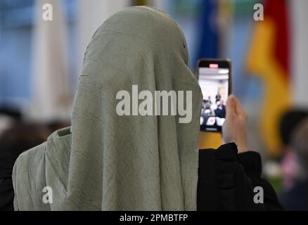 Magonza, Germania. 12th Apr, 2023. Una donna che indossa l'hijab scatta una foto durante un discorso prima di rompere il digiuno nella sala banchetti della Comunità islamica dei bosniaci (IGDB). Durante il mese del digiuno del Ramadan, le comunità musulmane della Renania-Palatinato invitano anche i non musulmani a rompere il loro digiuno (iftar) in serata. Credit: Arne Dedert/dpa/Alamy Live News Foto Stock