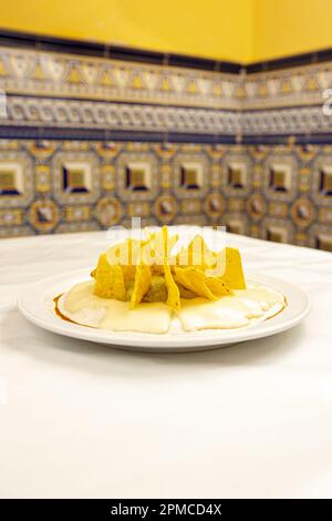 Un piatto di nachos con formaggio fuso e guacamole su un tavolo bianco Foto Stock