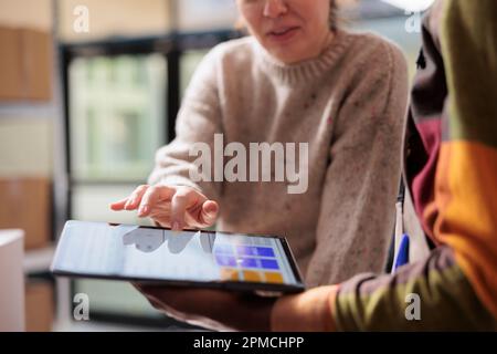 Colleghi del magazzino che analizzano gli ordini online sul tablet, preparando i pacchi per la spedizione in magazzino. Team eterogeneo che lavora all'inventario delle merci, scrivendo report su dispositivi digitali Foto Stock