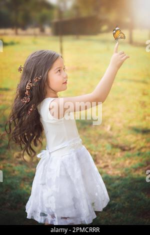 Ragazza in vestito bianco come una principessa, giocando con una farfalla, nella foresta con una favola, spazio copia, tema giorno per bambini. Foto Stock