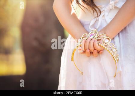 La bambina in vestito bianco è sulla schiena che tiene una corona principessa, in una foresta da sogno, spazio copia, tema giorno dei bambini. Foto Stock