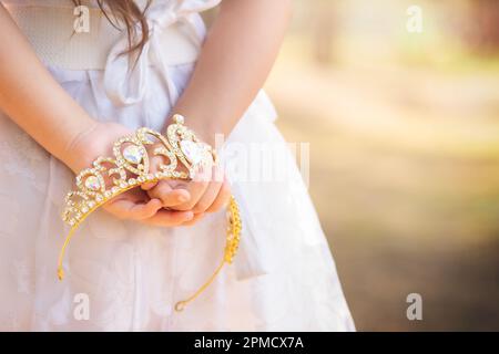 La bambina in vestito bianco è sulla schiena che tiene una corona principessa, in una foresta da sogno, spazio copia, tema giorno dei bambini. Foto Stock