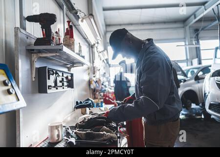 Vista laterale di un meccanico africano che lavora in garage, concetto meccanico a tiro medio. Foto di alta qualità Foto Stock