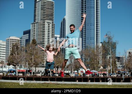 Divertente padre e figlio che saltano in città sullo sfondo. Concetto di bambino di infanzia e di paternità. Felice padre e figlio che giocano insieme all'aperto. Famiglie urbane. Foto Stock