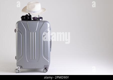 Valigia con cappello in paglia, occhiali da sole e macchina fotografica su sfondo bianco con spazio copia Foto Stock