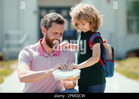 Pranzo scolastico per bambini. Il Padre sostiene e motiva il figlio. Scolaro e genitore in camicia che tiene il pranzo al sacco. Foto Stock