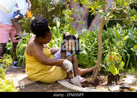 Nonna e nonna afroamericana che scavano la sporcizia con gli attrezzi mentre giardinaggio in iarda Foto Stock