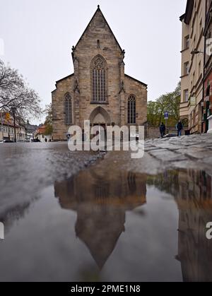 Erfurt, Germania. 12th Apr, 2023. La Predigerkirche si riflette in una pozza. Il 15 aprile 2023 si terrà nella Predigerkirche un rave techno sotto il motto "Rave Like God". La festa di ballo è prevista insieme alla gioventù protestante e al nightclub 'Kalif Storch'. Soprattutto i giovani sono da raggiungere, che altrimenti difficilmente hanno un legame con la chiesa. Oltre alla tariffa d'ingresso, i visitatori devono fare una donazione di cibo per la banca di cibo di Erfurt all'ingresso. Credit: Martin Schutt/dpa/Alamy Live News Foto Stock