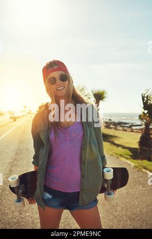 Vive per pattinare. una giovane donna che si aggrappa sul lungomare con il suo skateboard. Foto Stock