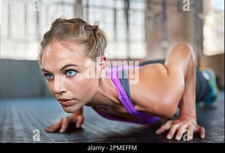 Il dolore è temporaneo, ma smettere dura per sempre. una giovane donna sportiva che fa i push-up in palestra. Foto Stock