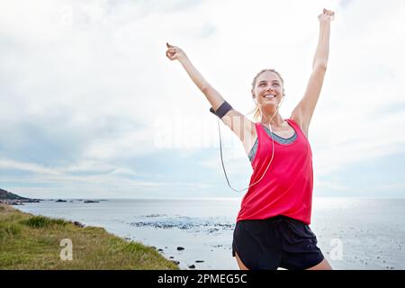 La migliore corsa di sempre. una donna con le braccia alzate in vittoria mentre fuori jogging vicino all'oceano. Foto Stock
