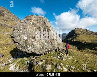 Collina femmina-walker in piedi sotto un enorme masso, Fionna Choire, Blaven, Isola di Skye, Scotland, Regno Unito Foto Stock