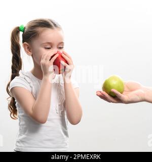 La bambina sceglie tra due mele, la mela rossa o verde, la scelta del bambino Foto Stock