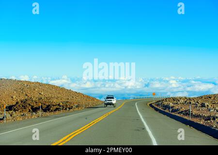 Un paesaggio mozzafiato di una strada tortuosa lungo una scogliera con una ringhiera, alta sopra le nuvole, e una macchina che si avvicina verso lo spettatore. Foto Stock