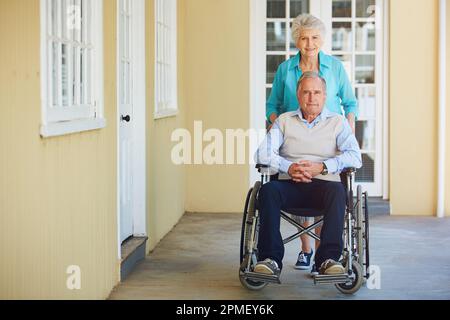 Sostegno sponsale negli anni più anziani. Ritratto di una donna anziana che spinge il marito su una sedia a rotelle in una casa di riposo. Foto Stock