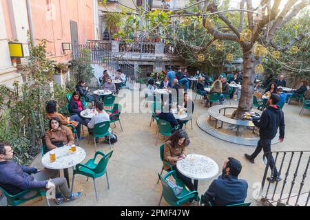 Barcellona, Spagna - 13 marzo 2023: Persone sedute fuori al bar in una piccola piazza. Edifici tradizionali e albero decorativo Foto Stock