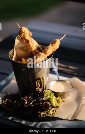 Patatine fritte e carne su bastoncini di legno serviti in un secchio di metallo con salsa e verdure Foto Stock
