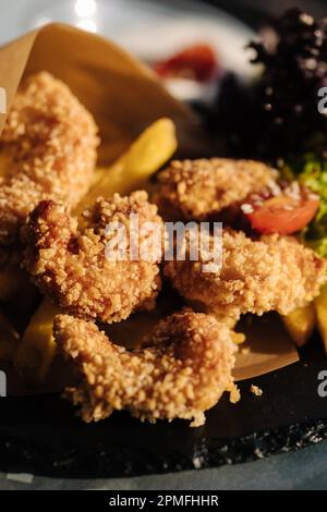 Gamberetti fritti in pangrattato serviti in carta alimentare su piatto Foto Stock