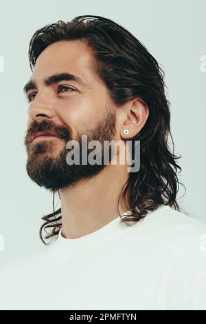 Uomo caucasico sicuro in piedi in uno studio, con un look di auto-assicurazione sul suo volto. Giovane uomo con pelle e capelli perfetti abbraccia il suo beau Foto Stock