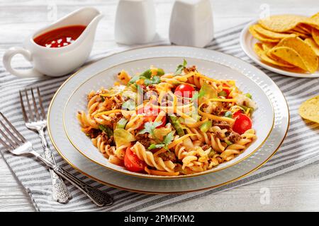 Insalata di pasta Nacho con carne macinata, pomodori, peperoni verdi, lattuga iceberg e condimento taco in ciotola bianca su tavola di legno bianco Foto Stock