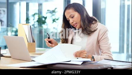 Agente pubblicitario femminile che guarda occupato mentre parla durante una chiamata telefonica e la ricerca attraverso i documenti su una tabella disordinata in un ufficio. Marketing femminile Foto Stock
