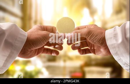 Le mani di un sacerdote consacrano un'ostia come corpo di Cristo per distribuirla ai comuni della chiesa Foto Stock