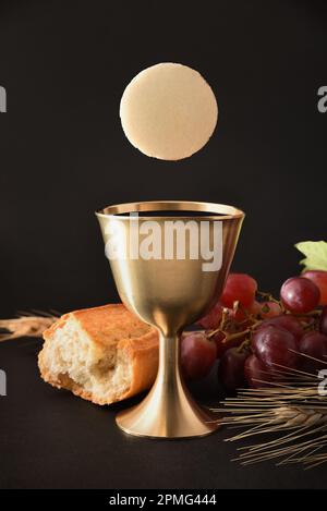 Ricordo della prima comunione con una calice e un ostia su una tavola nera con un pane mazzetto di uva e orecchie di grano. Compos. Verticale Foto Stock