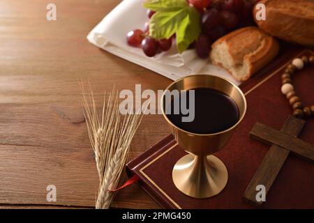 Coppa di vino e ostie su tavola di legno con bibbia e candela per eucaristia sfondo nero isolato. Vista frontale. Foto Stock