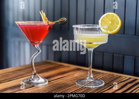 Cocktail alcolici Cosmopolitan e Margarita su tavolo di legno contro parete scura con spazio copia Foto Stock