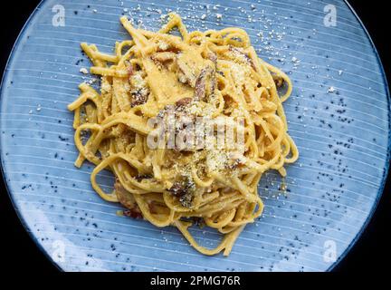 Pasta carbonara con pancetta su piatto blu isolato su sfondo nero vista dall'alto Foto Stock