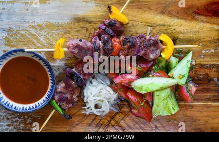 Spiedini di maiale serviti con insalata e salsa su sfondo nero vista dall'alto Foto Stock