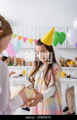 ragazza stupita in testa festa ricevendo regalo di compleanno da un amico su sfocato in primo piano, immagine di scorta Foto Stock