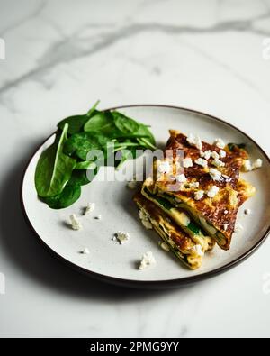 Frittata ripiegata ripiena di spinaci e feta sul piatto bianco con foglie di spinaci sul retro. Colazione sana e dietetica. Cibo minimalista Foto Stock