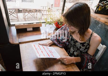 etnicità transgender argentina giovane donna latina prendere decisioni in ristorante, lettura menu, sedersi a tavola, business concept, spazio copia. Foto Stock
