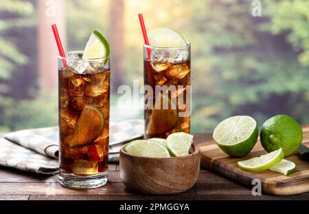 Cocktail al rum e alla cola con fettina di lime su un tavolo rustico in legno con sfondo estivo e spazio copia Foto Stock