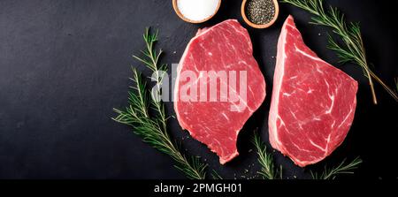 Due carni fresche di marmorizzata crude, bistecche di angus nero, aglio, sale e su fondo scuro. Due classiche bistecche fresche di costolette sulla tavola di ardesia. Bistecche di manzo Foto Stock