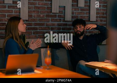 Coppia simpatica seduta insieme al caffè, sorridendo parlando e facendo una discussione su qualcosa, spiegando le mani di spirito Foto Stock