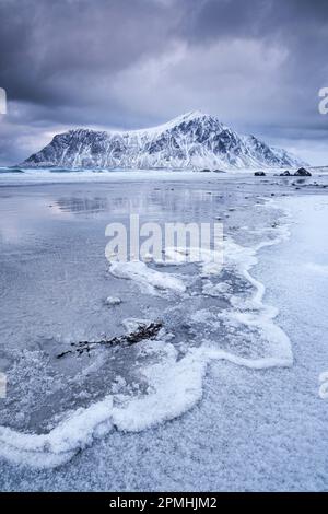 Frozen Wave Patterns sulla spiaggia di Skagsanden sostenuta da Hustinden montagna inverno, vicino Flakstad, Flakstadoya, Lofoten isole, contea di Nordland, Norvegia, SC Foto Stock